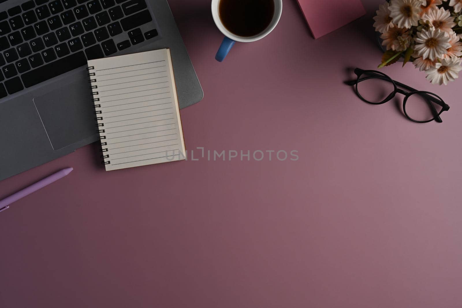 Top view notepad, laptop computer, eyeglasses and coffee cup on purple background.