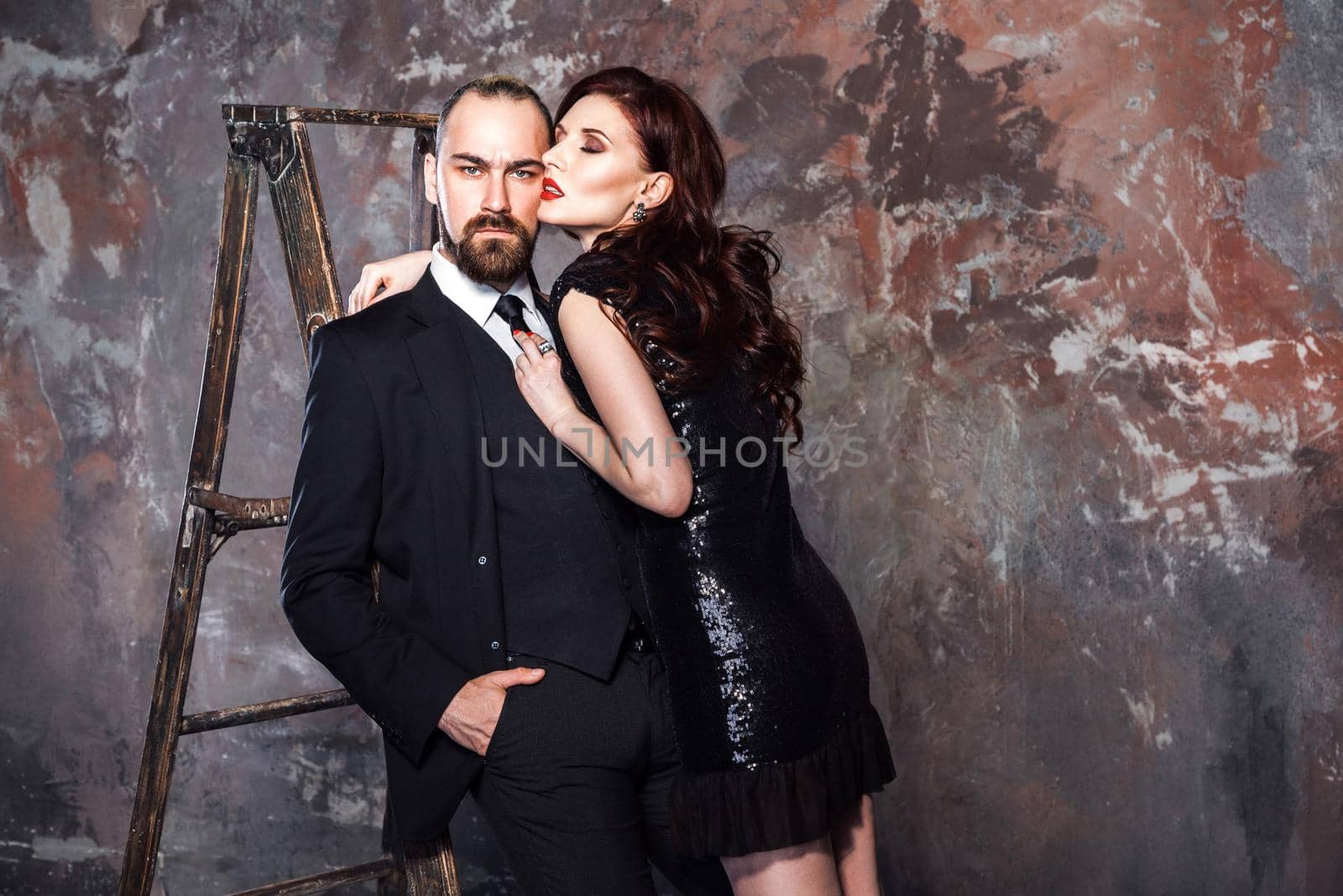 Closeup bearded blonde businessman and foxy woman standing near stepladder. Studio shot, isolated on shabby wall