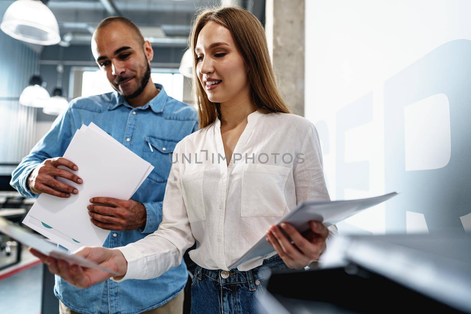 Two employees using new modern printer in office by Fabrikasimf