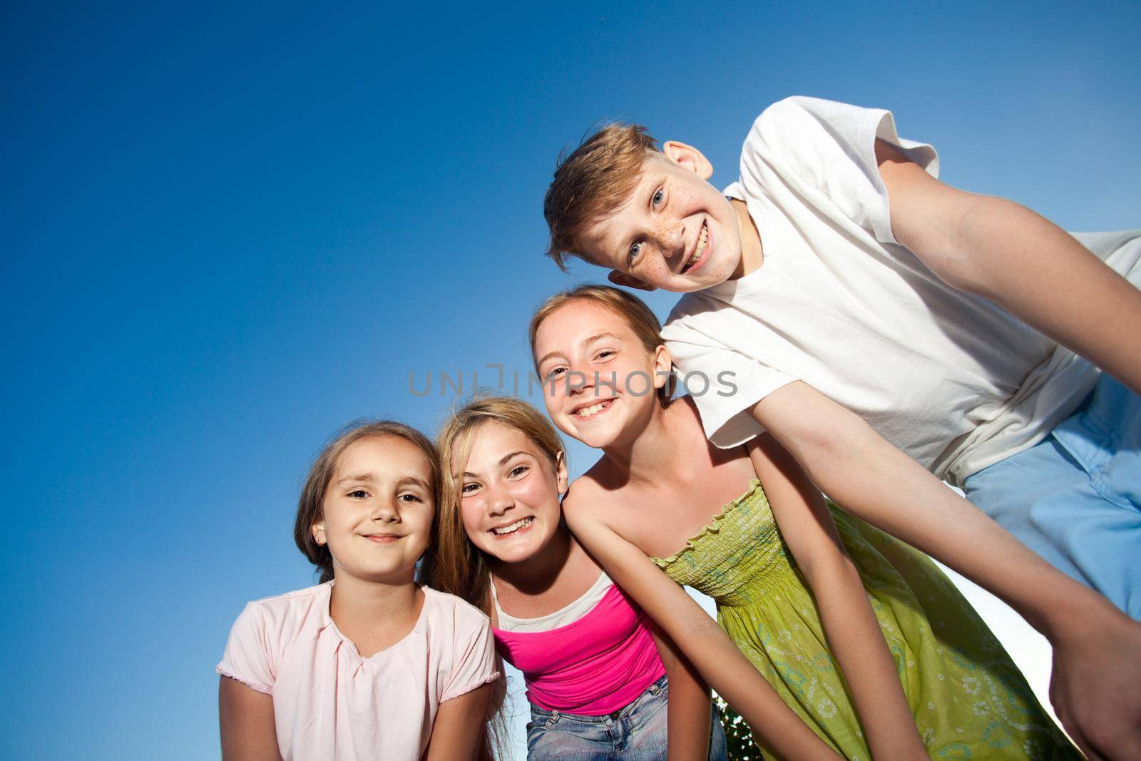 four happy beautiful children looking at camera from top in the sunny summer day and blue sky. looking at camera with funny face and toothy smile. view from below.