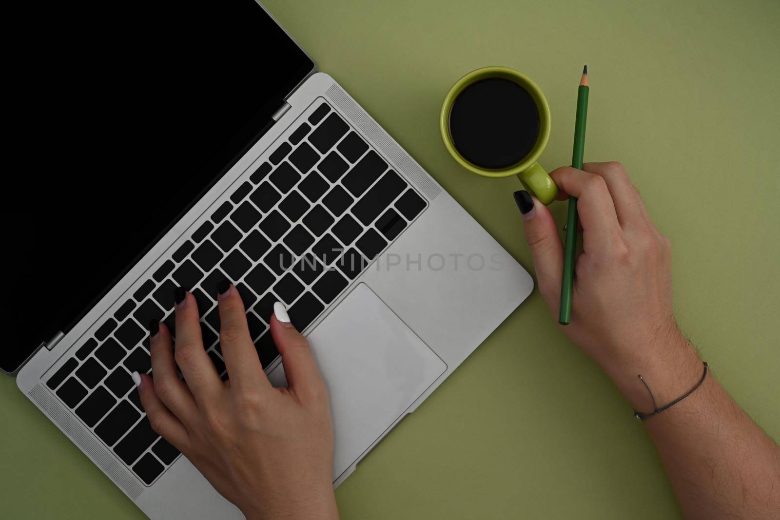 Female designer holing coffee cup and using computer laptop over green background.