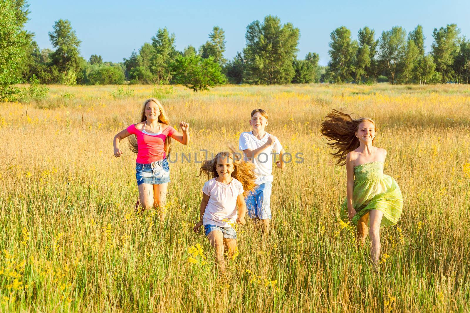 four happy beautiful children running playing moving together in the beautiful summer day. jumping and looking at camera with happiness and toothy smile.