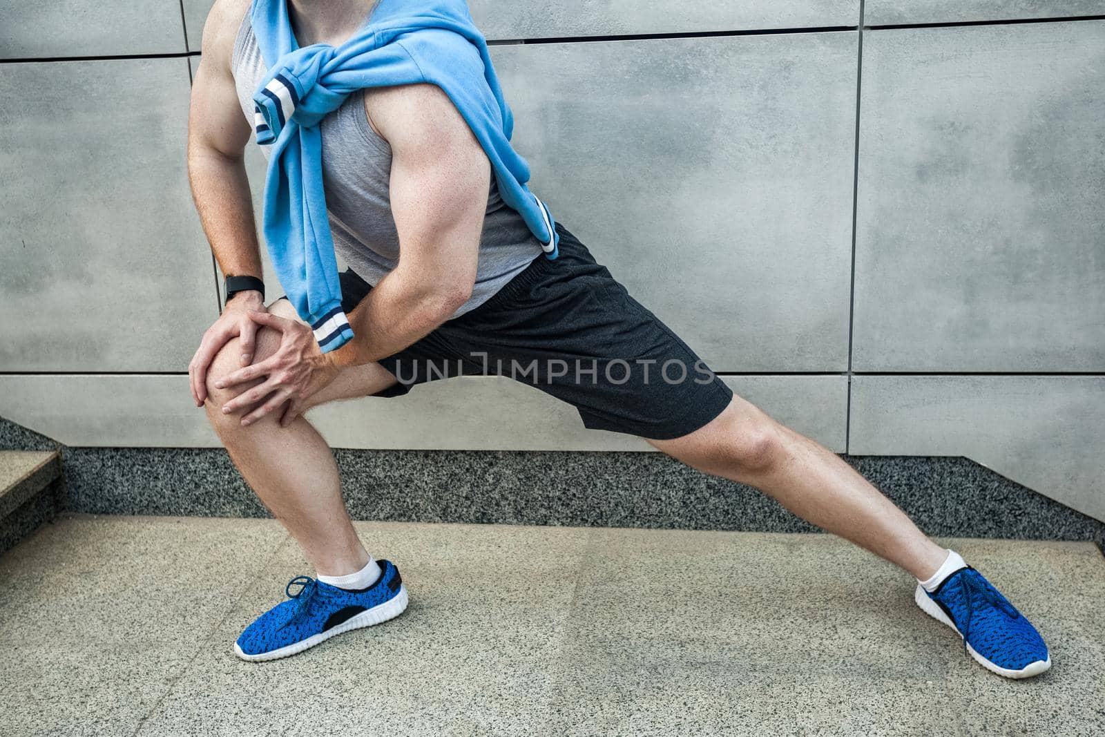Fitness young man in sportswear doing yoga fitness exercise in the city street over gray concrete background. Outdoor sports clothing and shoes, urban style. Sneakers close up.