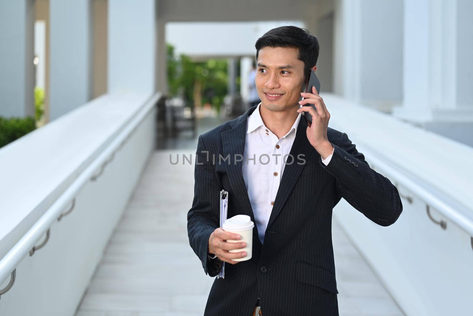 Handsome asian male entrepreneur in formal clothes having phone conversation and walking through office building. Business, lifestyle concept.