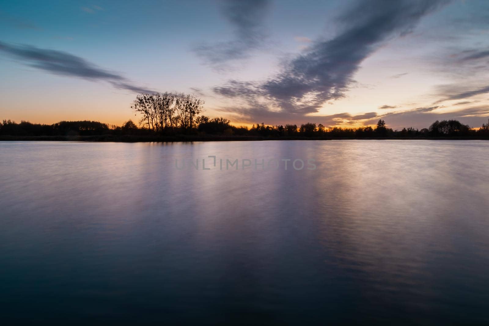 Evening colourful clouds after sunset over a calm lake, autumn view, long time exposure