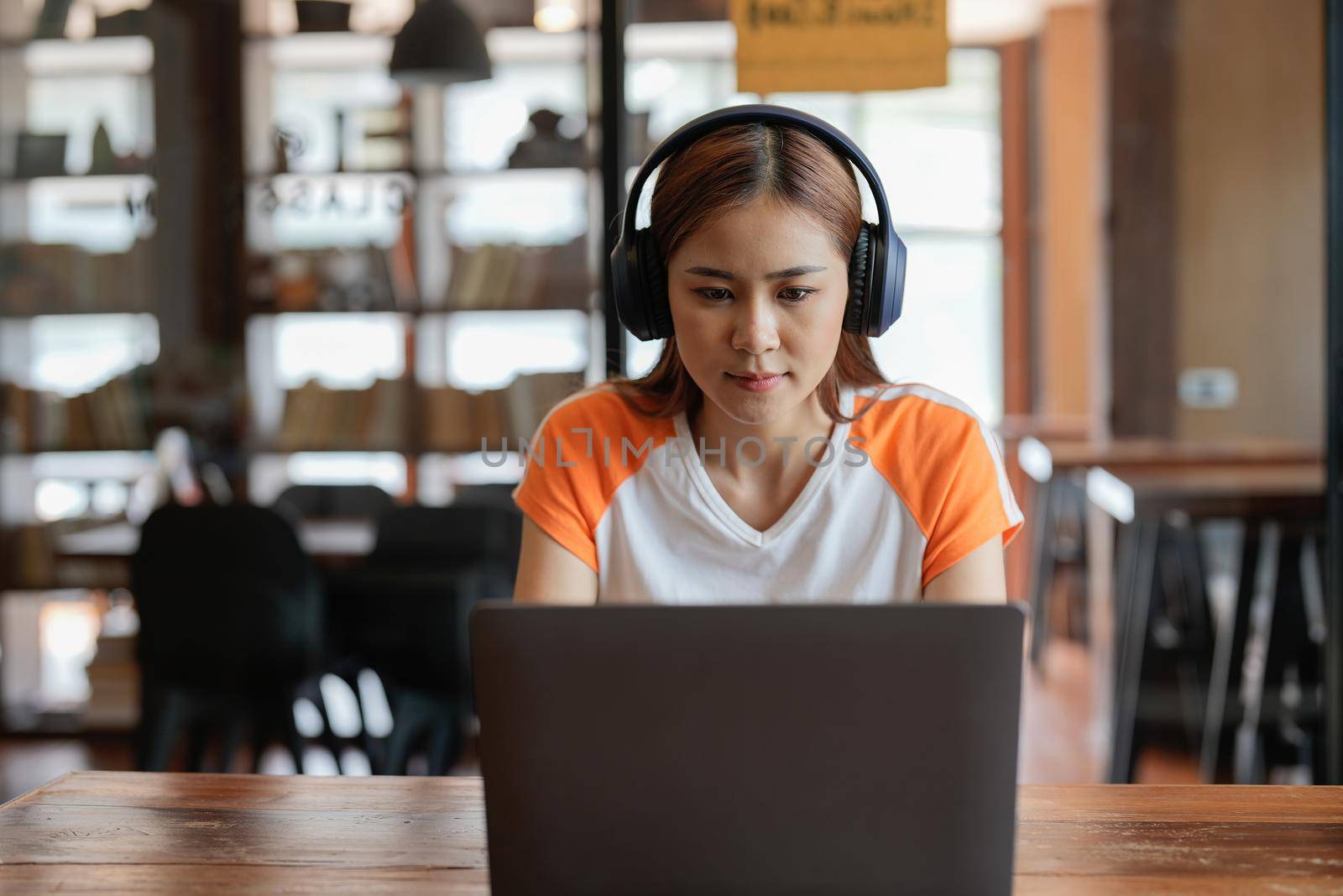 Seriously teenage asian female remote student sit by home computer participate at virtual event distant lesson. Confident young biracial woman in earphones teach study foreign language online.