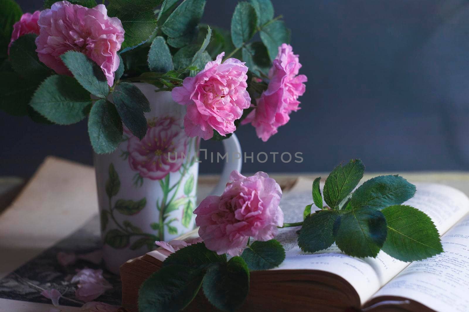 An old book with a bouquet of ancient roses in a vintage cup, summer reading concept, selective focus