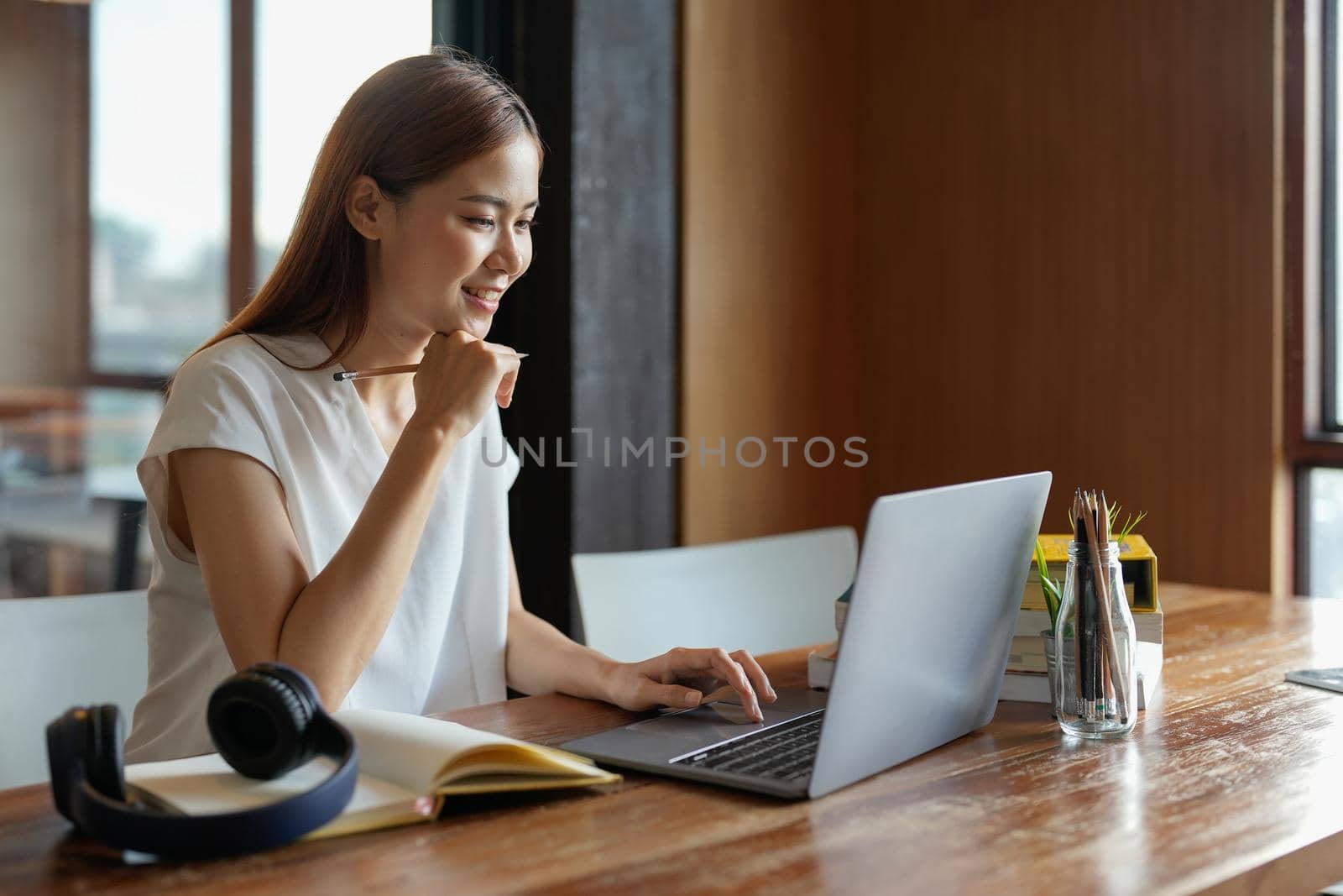 Pensive young asian woman in headphones work on laptop talk speak on video webcam call online. Smart ethnic female in earphones study distant on computer at home. Education concept. by nateemee