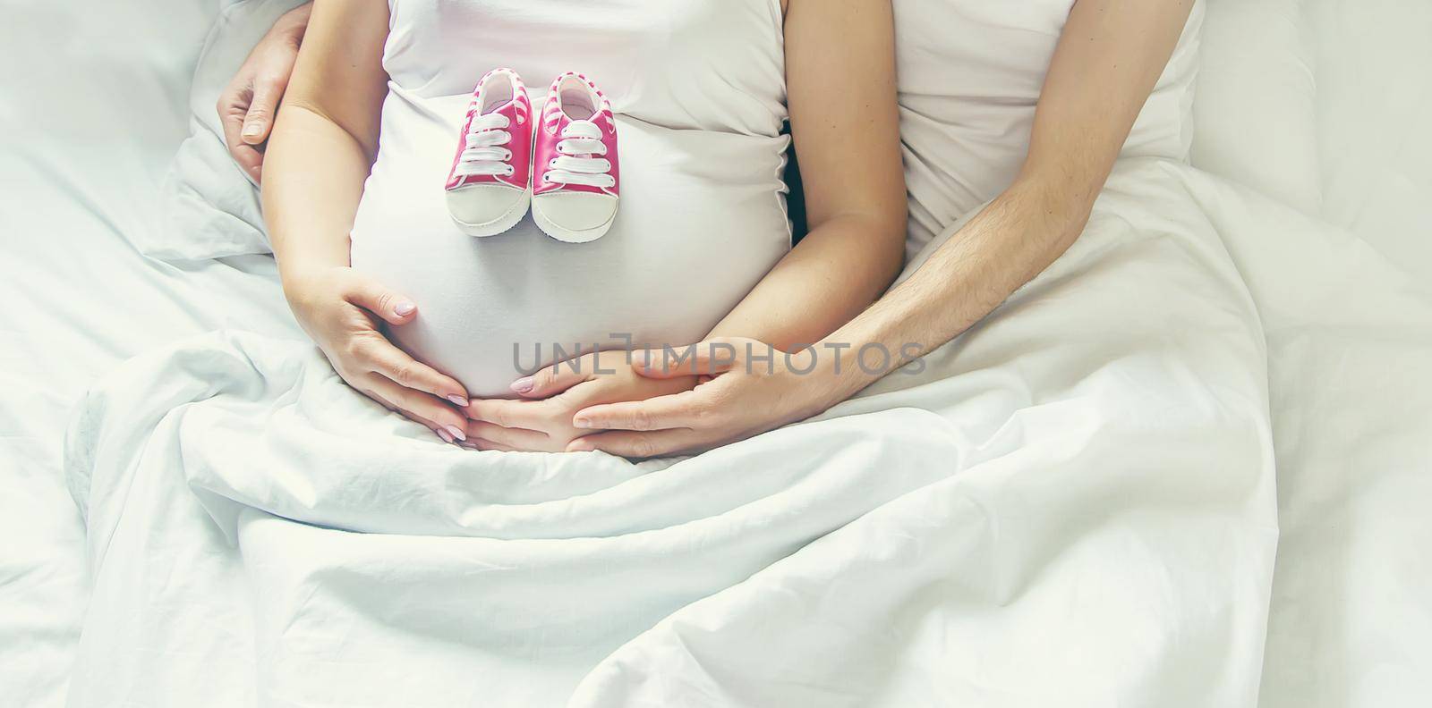 Pregnant woman and man hug belly and hold baby shoes. Selective focus. by yanadjana