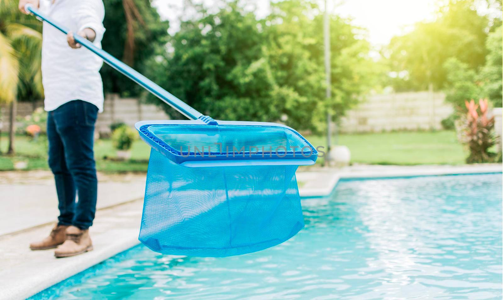 Man cleaning the pool with the Skimmer, A man cleaning pool with leaf skimmer. Person with skimmer cleaning pool, Hands holding a skimmer with blue pool in the background