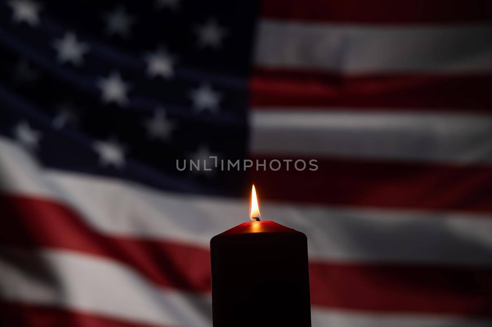 Burning candle against the background of the waving flag of the united states of america in the dark