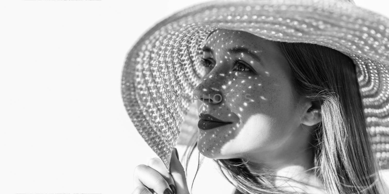 Profile side view portrait of happy dreamy beautiful young woman with hat looking away and smiling, holding hat, light through hat falls on face. Indoor, studio shot isolated on background copyspace.