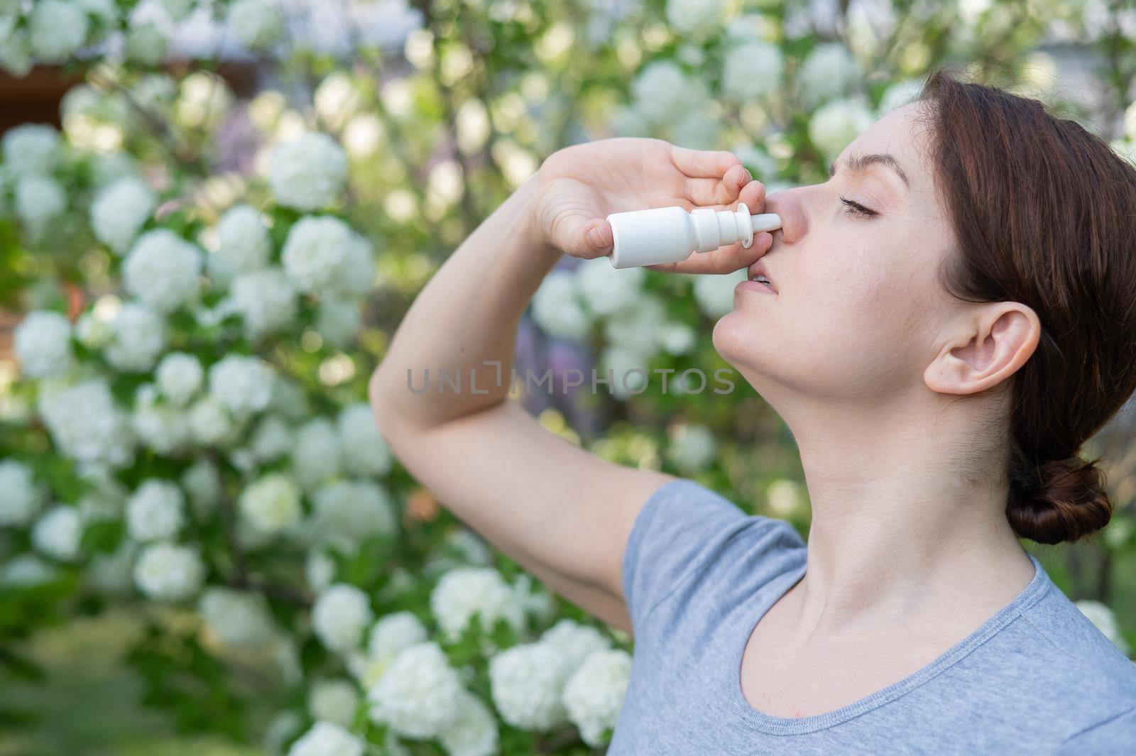 Caucasian woman uses a nasal spray while walking in the park. by mrwed54