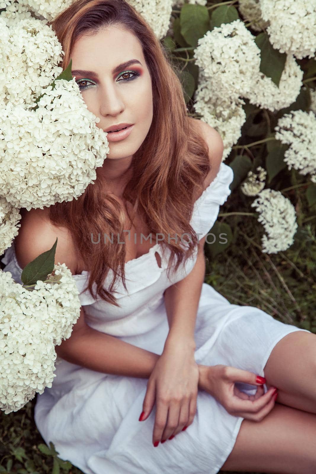 View from above. Handsome young adult woman sitting near many flowers in park. Outdoor spring or summer photo