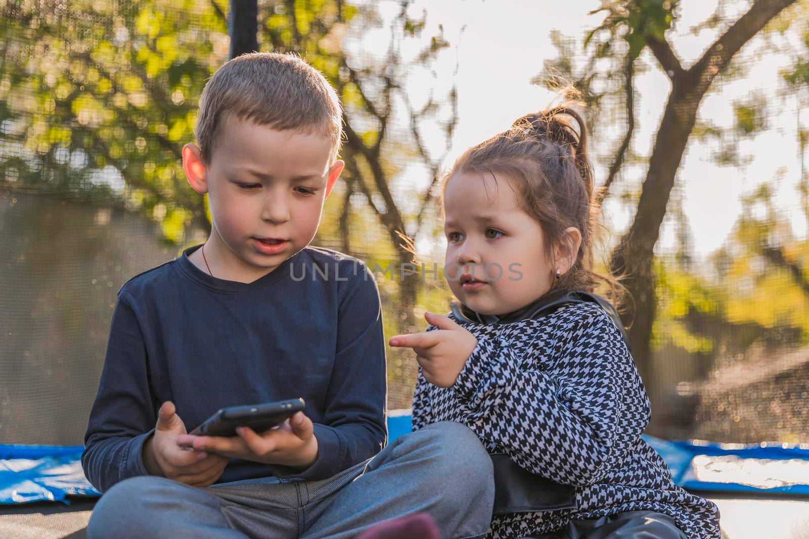 children sit on a trampoline and look at the phone