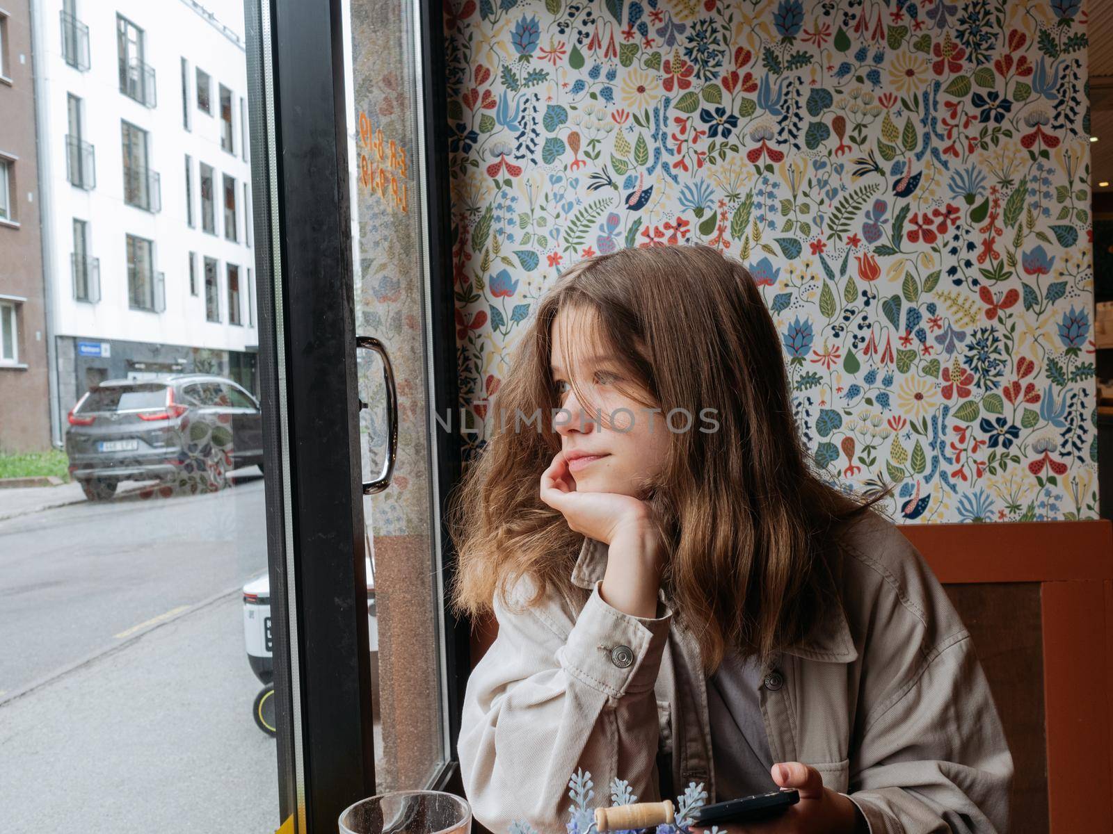Portrait of a young girl sitting at the window of the cafe with a calm smile