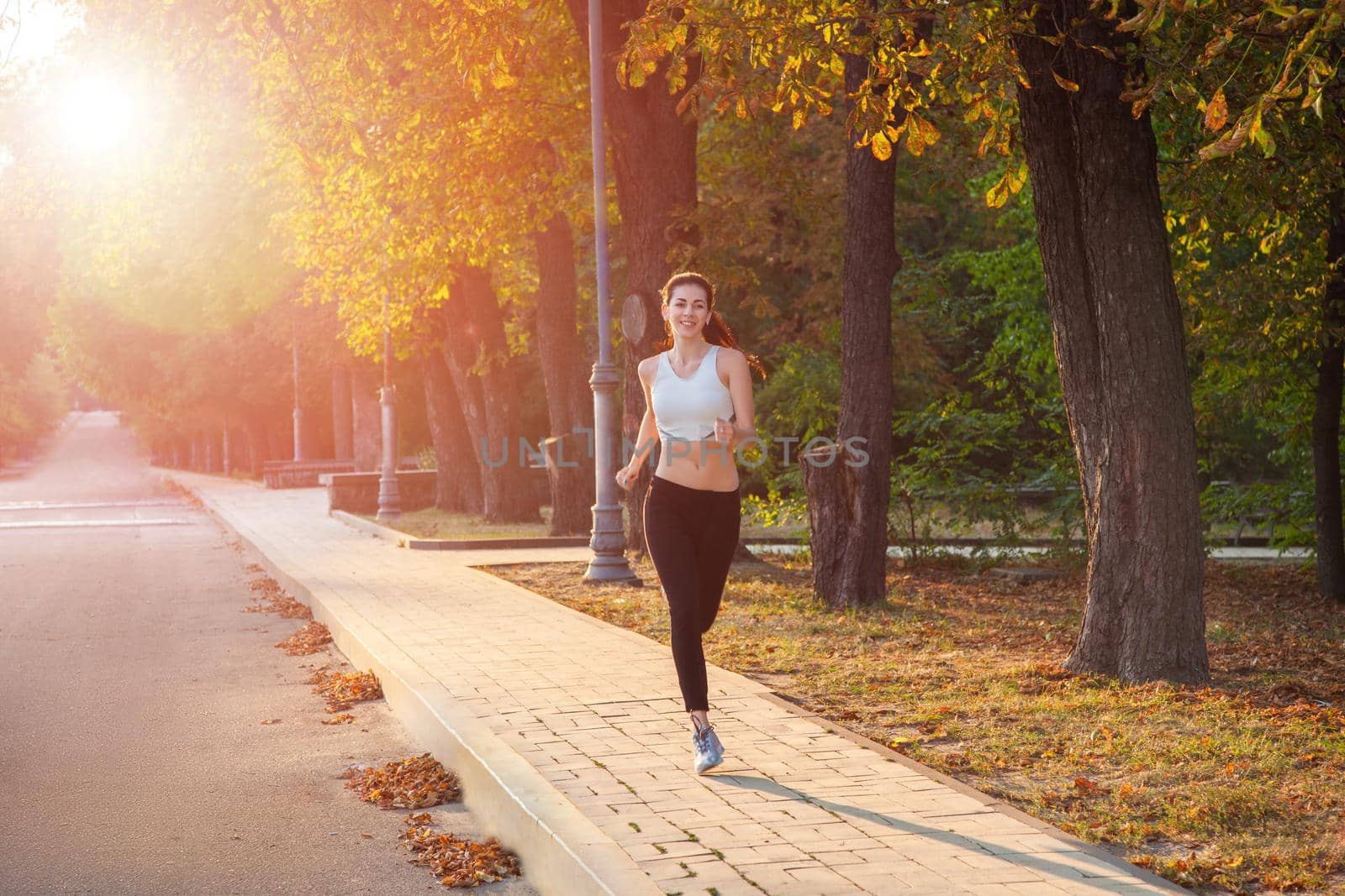 young beautiful happy and sexy runner girl with nice body in the autumnal colored park. with sun on backlight is looking at camera with happiness and smile with white sport suit. by Khosro1