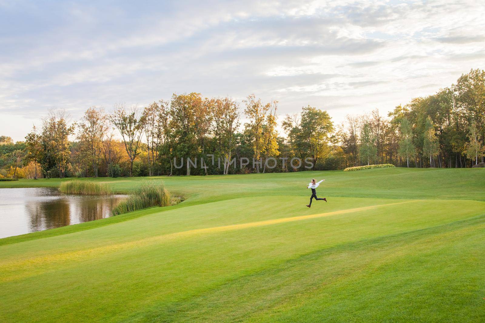 Young adult girl runs on the green grass of the golf course. The girl happiness. by Khosro1