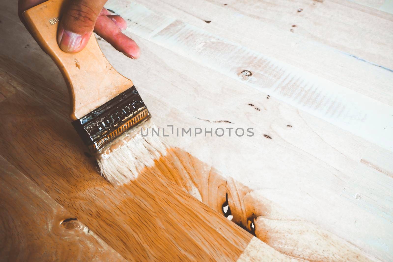Applying varnish paint on a wooden surface. Man hand with a brush closeup to process finishing material in construction by Petrichor