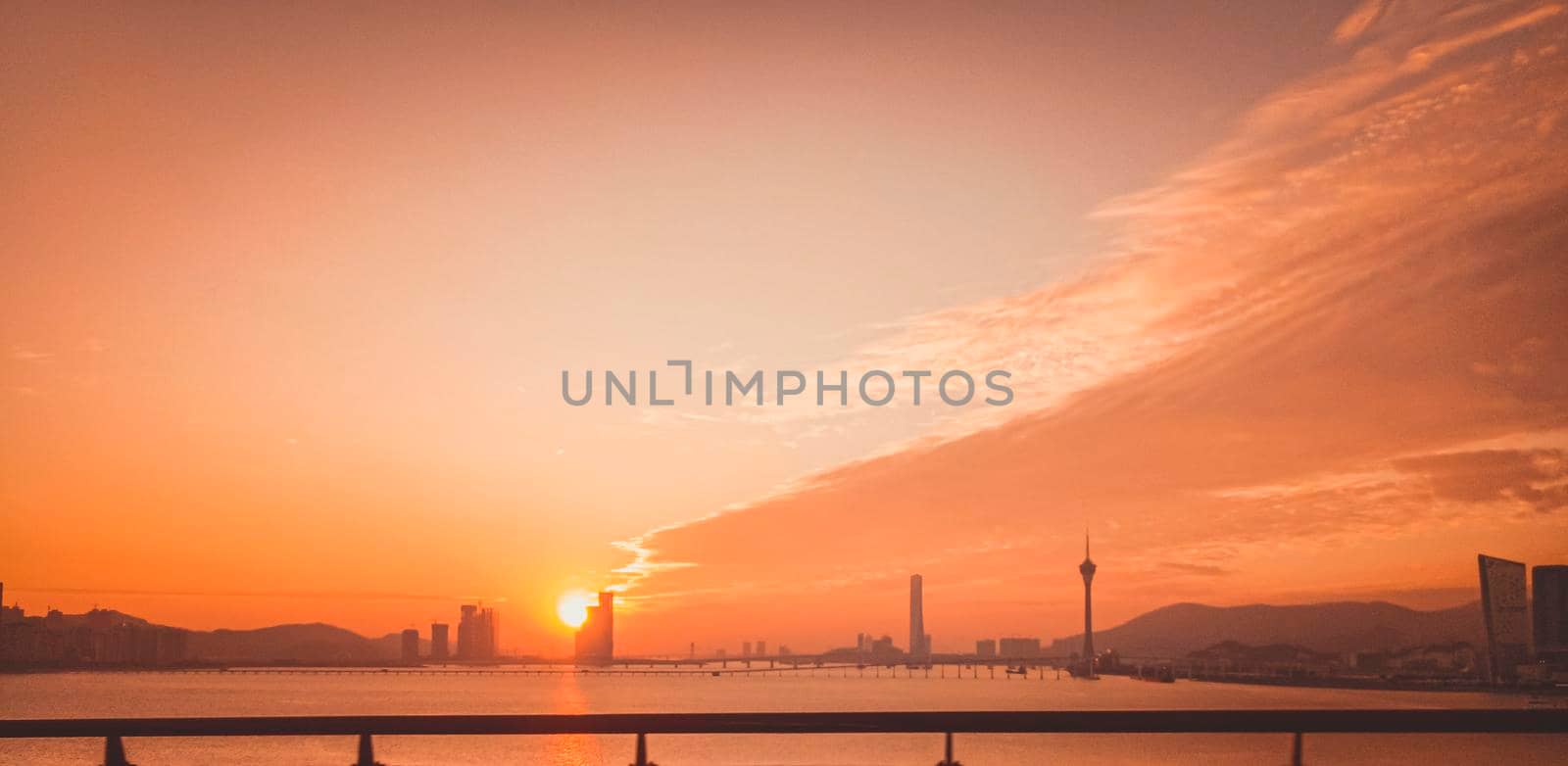 Urban landscape of Macau with famous traveling tower under orange sunset sky near river in Macao, Asia