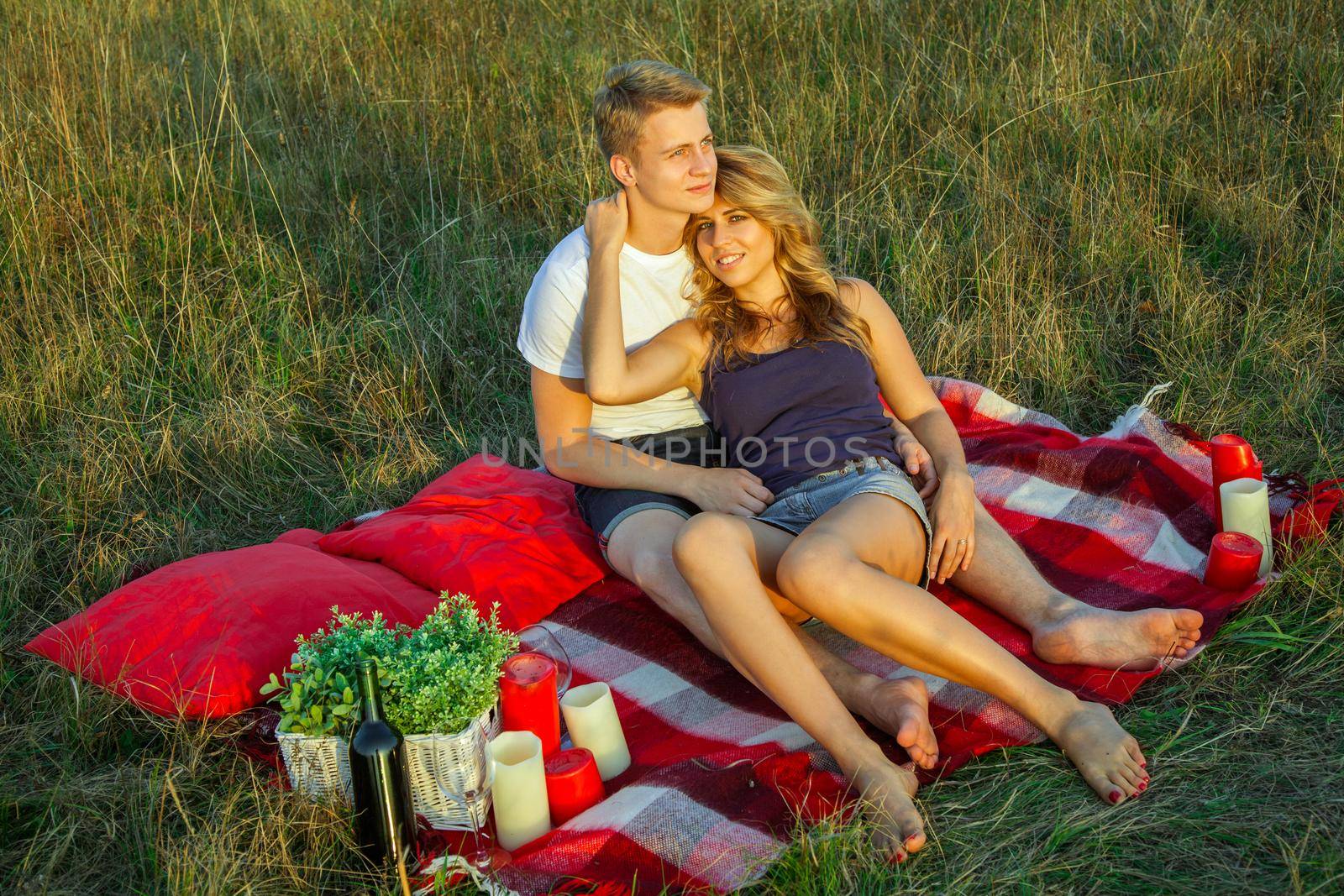 Beautiful young happy loving couple on picnic lying down on plaid in field on sunny summer day enjoying and resting. looking at camera and smiling. top view.