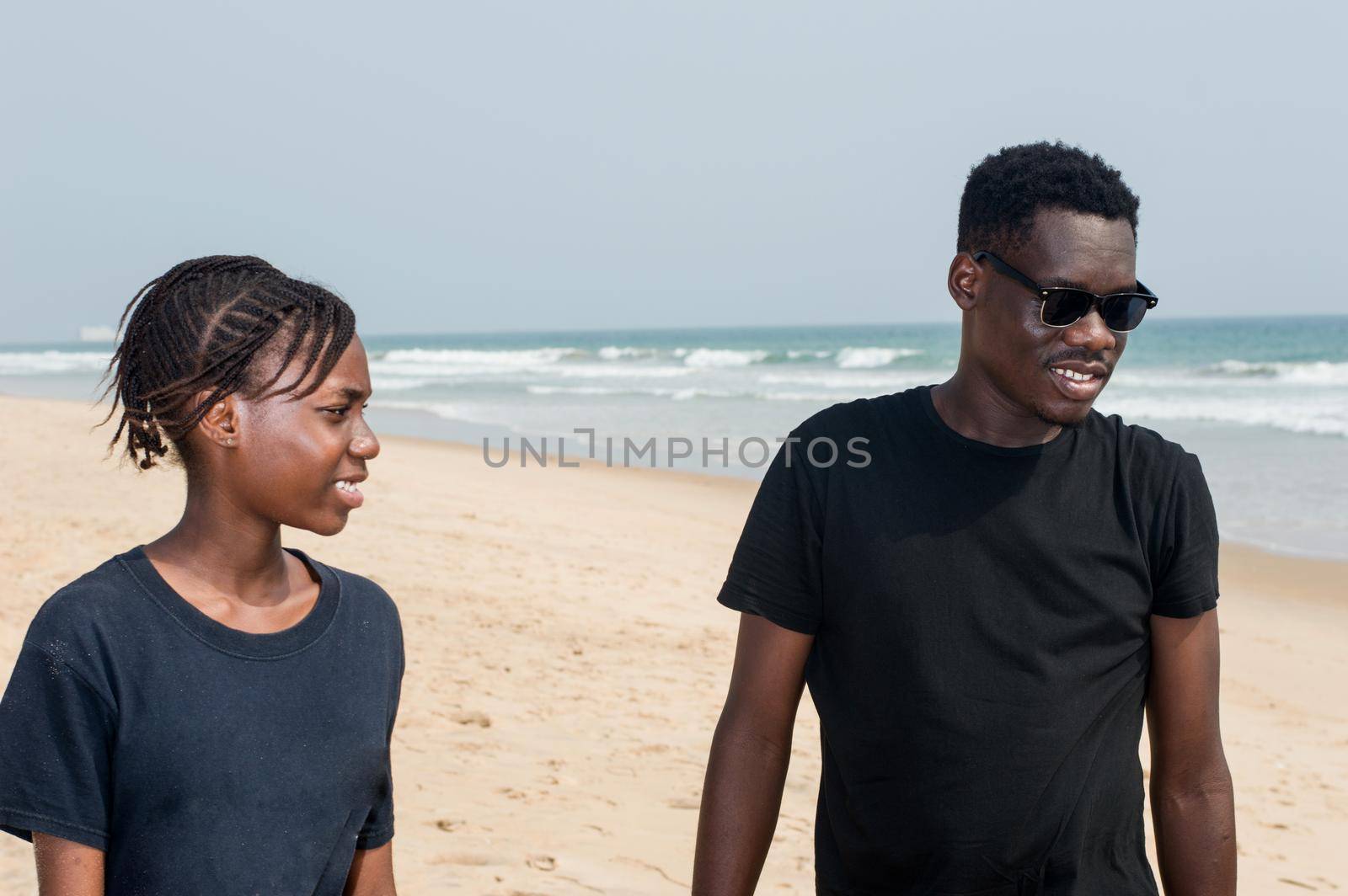two young people one in black tee shirt and the other in blue t-shirt standing at the beach smiling.