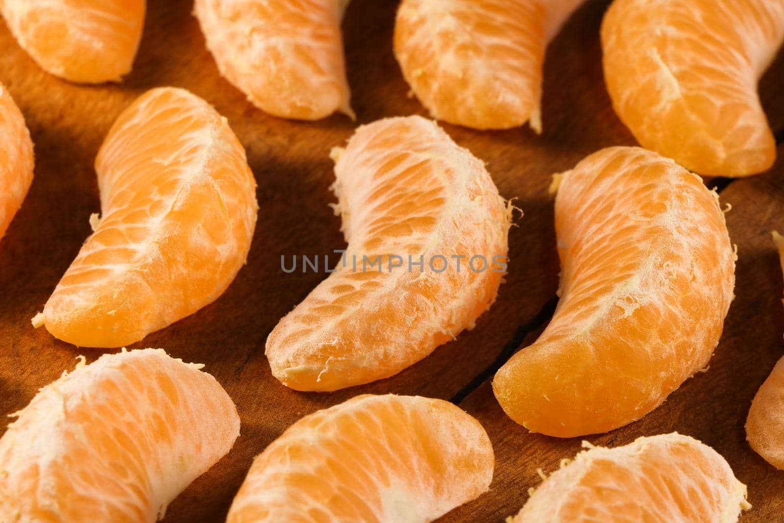 Fresh satsuma mandarin tangerine (Citrus unshiu) fruit wedge layout on natural wood surface abstract, South Africa