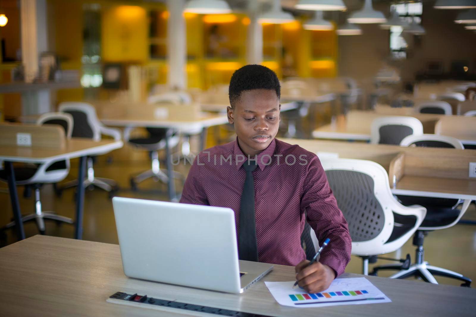 portrait of contemporary African-American man using laptop sitting at table in coffee shop, copy space