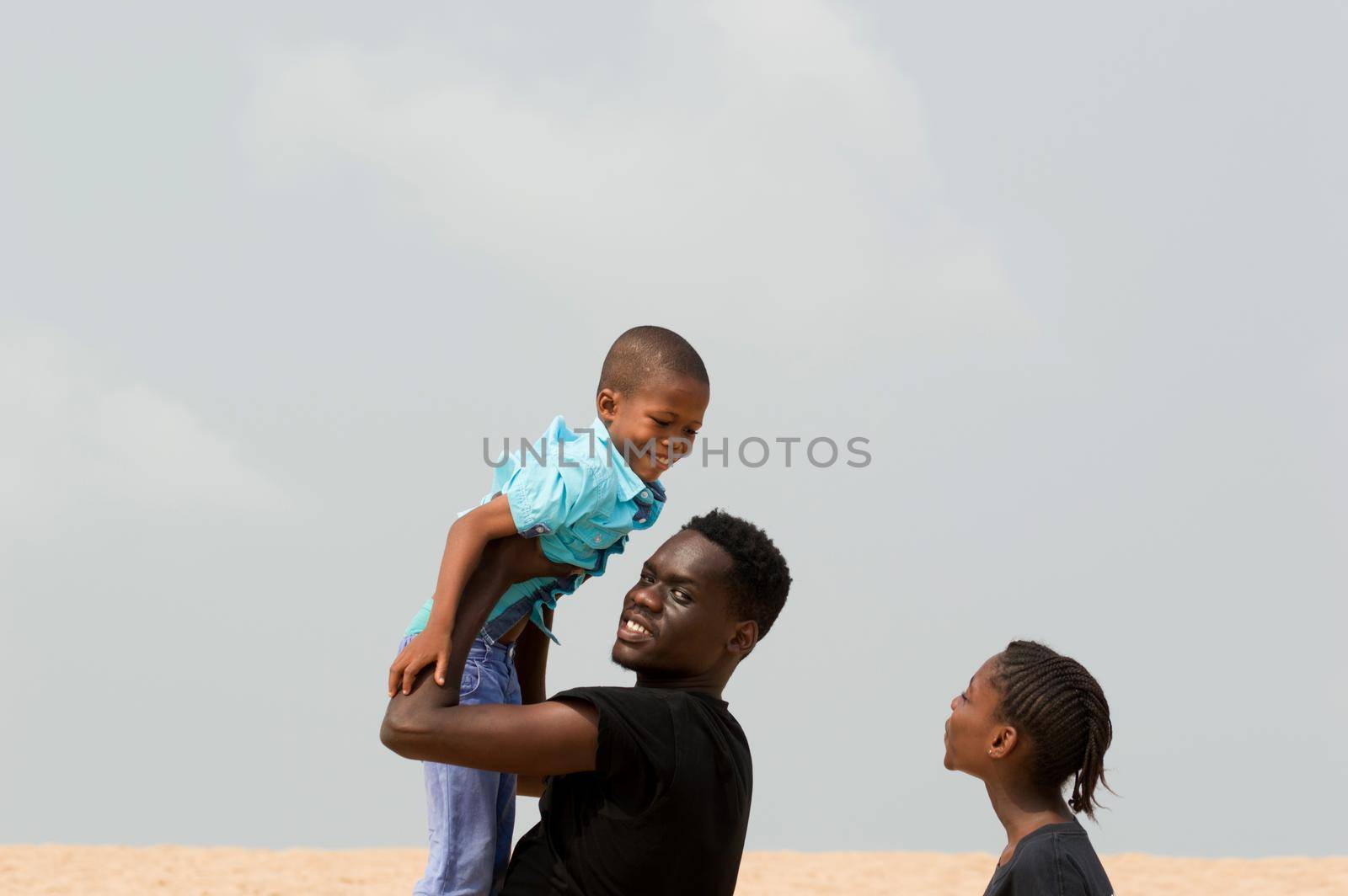 young man raising his little brother and little sister looks at them smiling.