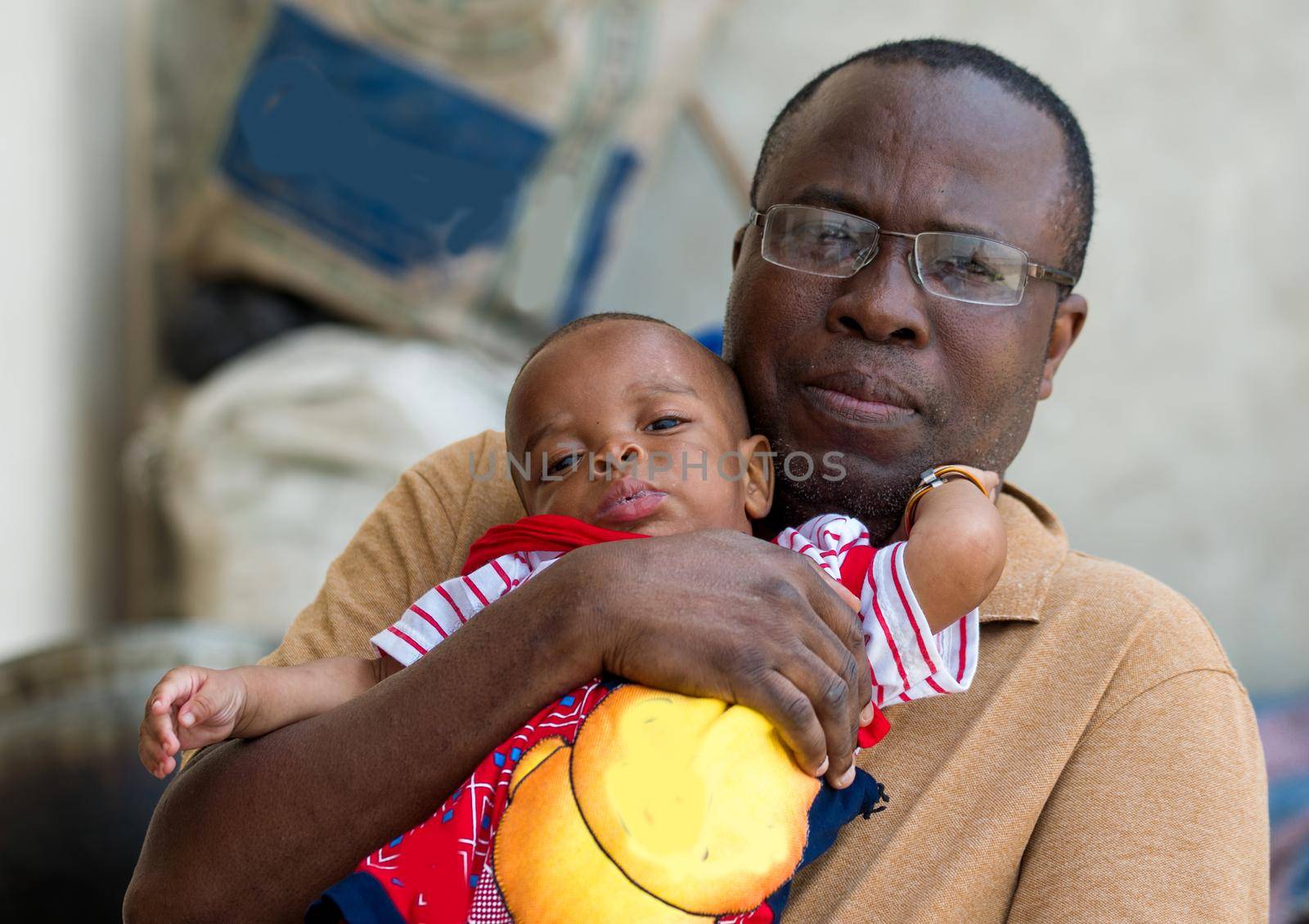 a man in glasses sitting outside holds his baby in his hands.
