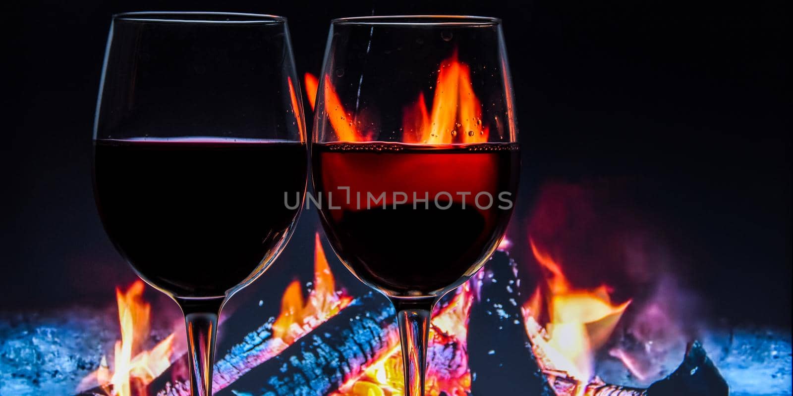 A glass of wine against the background of a burning fire. The atmosphere of rest and relaxation. Water drops, banner, christmas holiday, winter