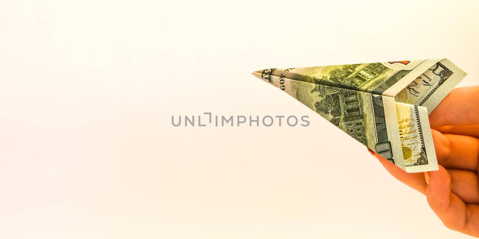 A female hand and folded paper planes origami made by USD notes bills, copy space for text, paper aircraft launching isolated on white, travel and money