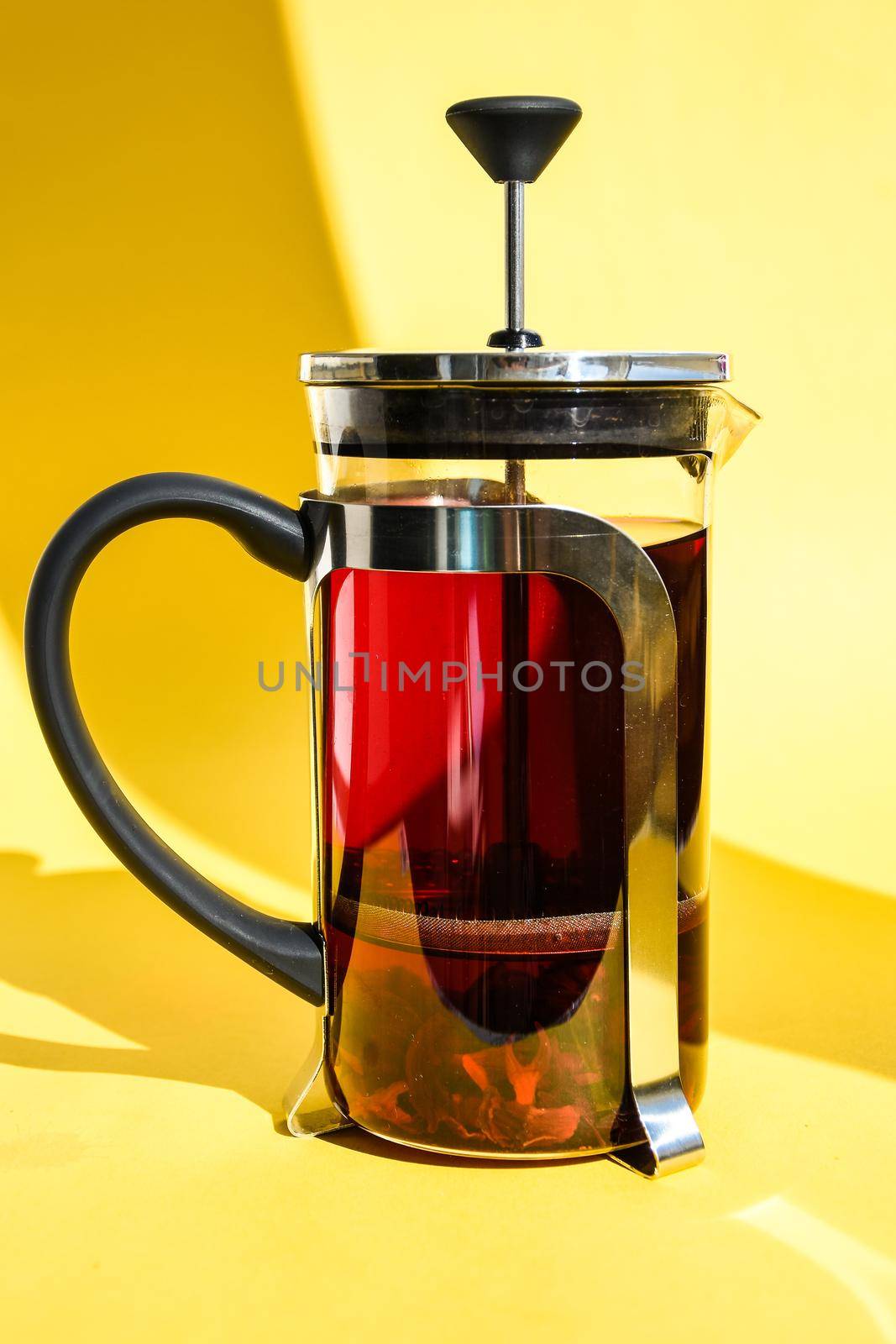 Fresh brewed spicy fruit tea with herbs, rose flowers, hot healthy drink on yellow background with copy space for text, Hibiscus tea, flower and dry blossom, glass teapot with hot tea