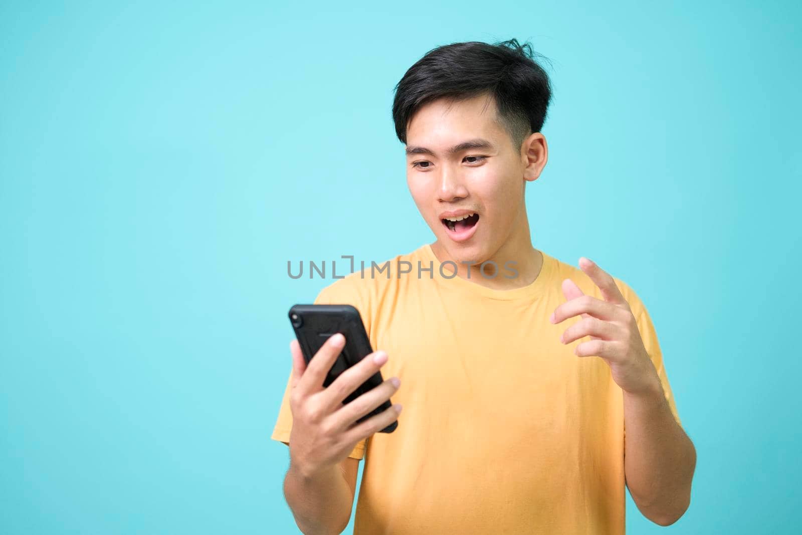 Portrait of a shocked young man using mobile phone isolated over blue background.