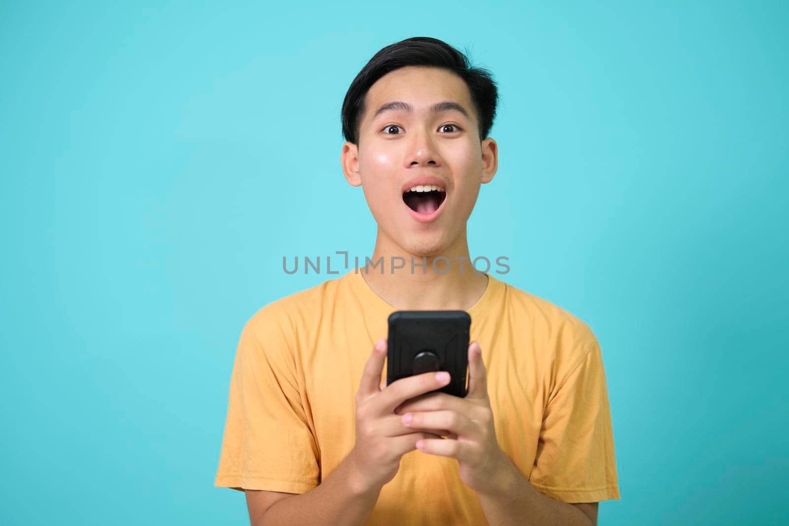 Portrait of a shocked young man using mobile phone isolated over blue background.