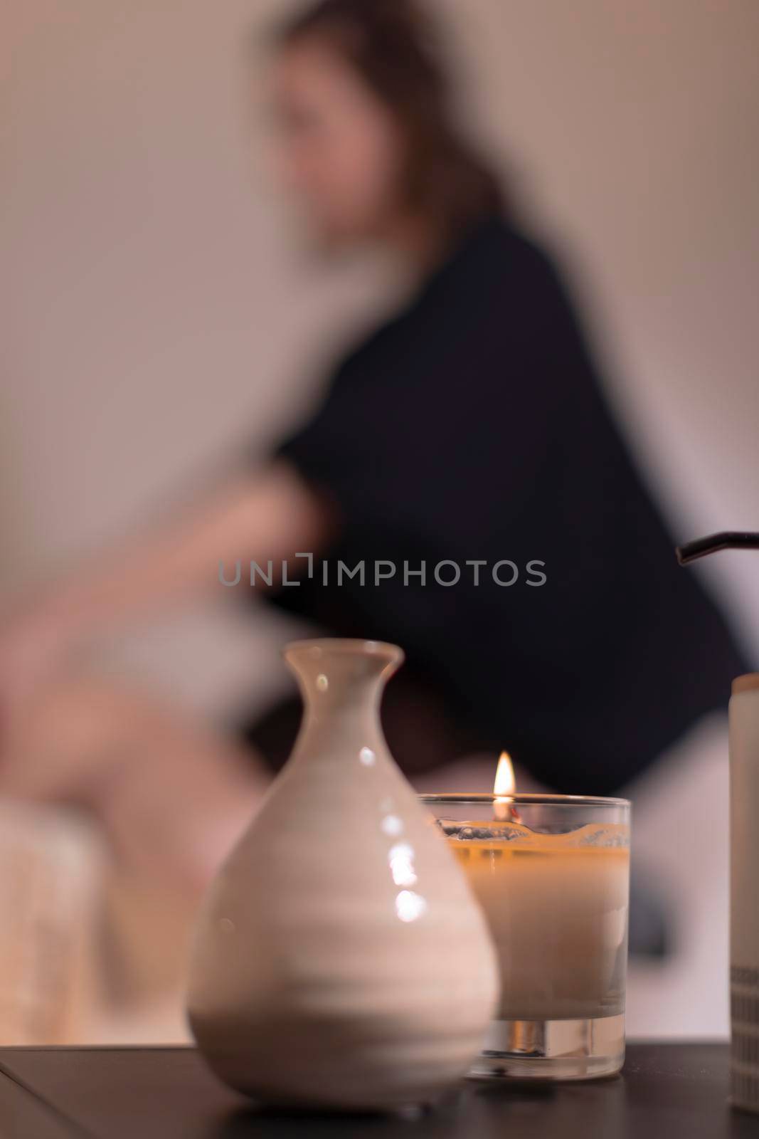 An aromatic candle dominates the scene while in the background a therapist massages her patient to relieve her muscle pain