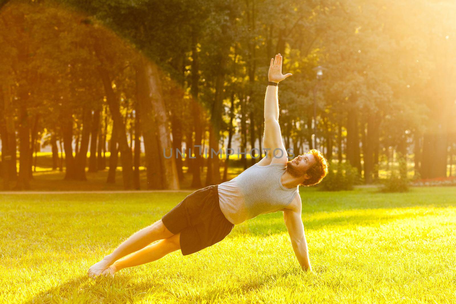 Strong young adult man doing yoga. Stay in plank on one arm. Looking up to the sky. Outdoor shot