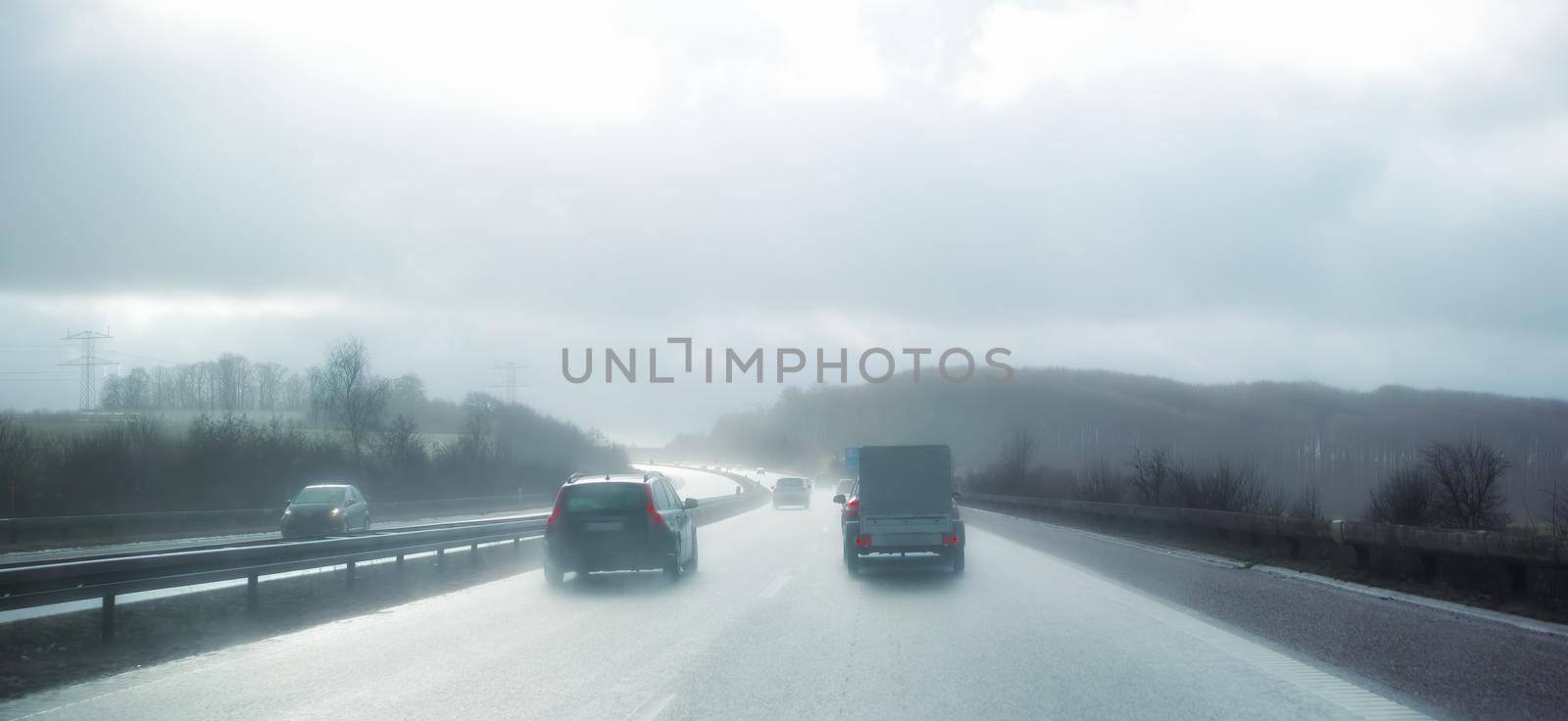 Cars at breaking distance on a highway on a rainy day in Denmark. Motor vehicles driving on a dangerous asphalt road on a cold misty winter day in a picturesque landscape. Safe driving in bad weather.