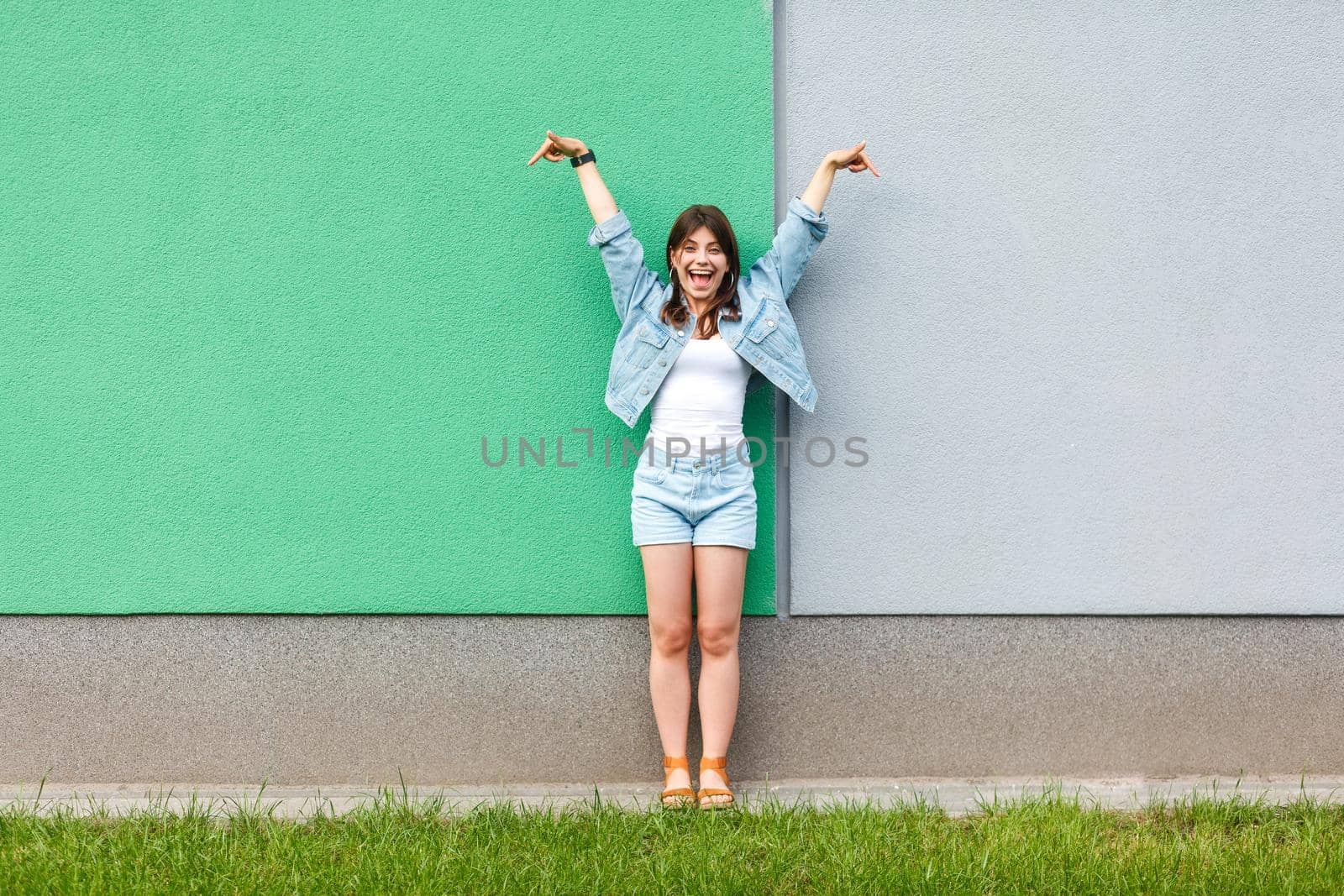 Full length portrait of excited beautiful woman in casual jeans denim style in summertime standing and pointing at green and light blue wall copyspace. two different choice concept.