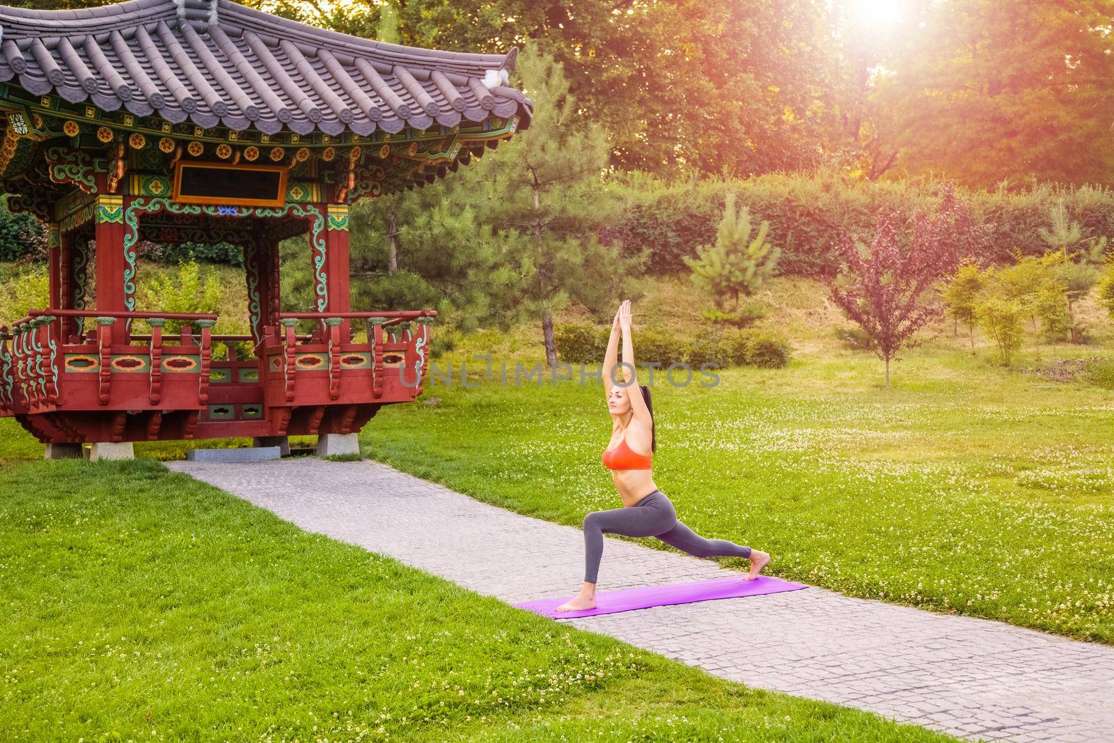 Cheerful young beautiful woman practicing and posing yoga in the east Asian park. warrior pose.