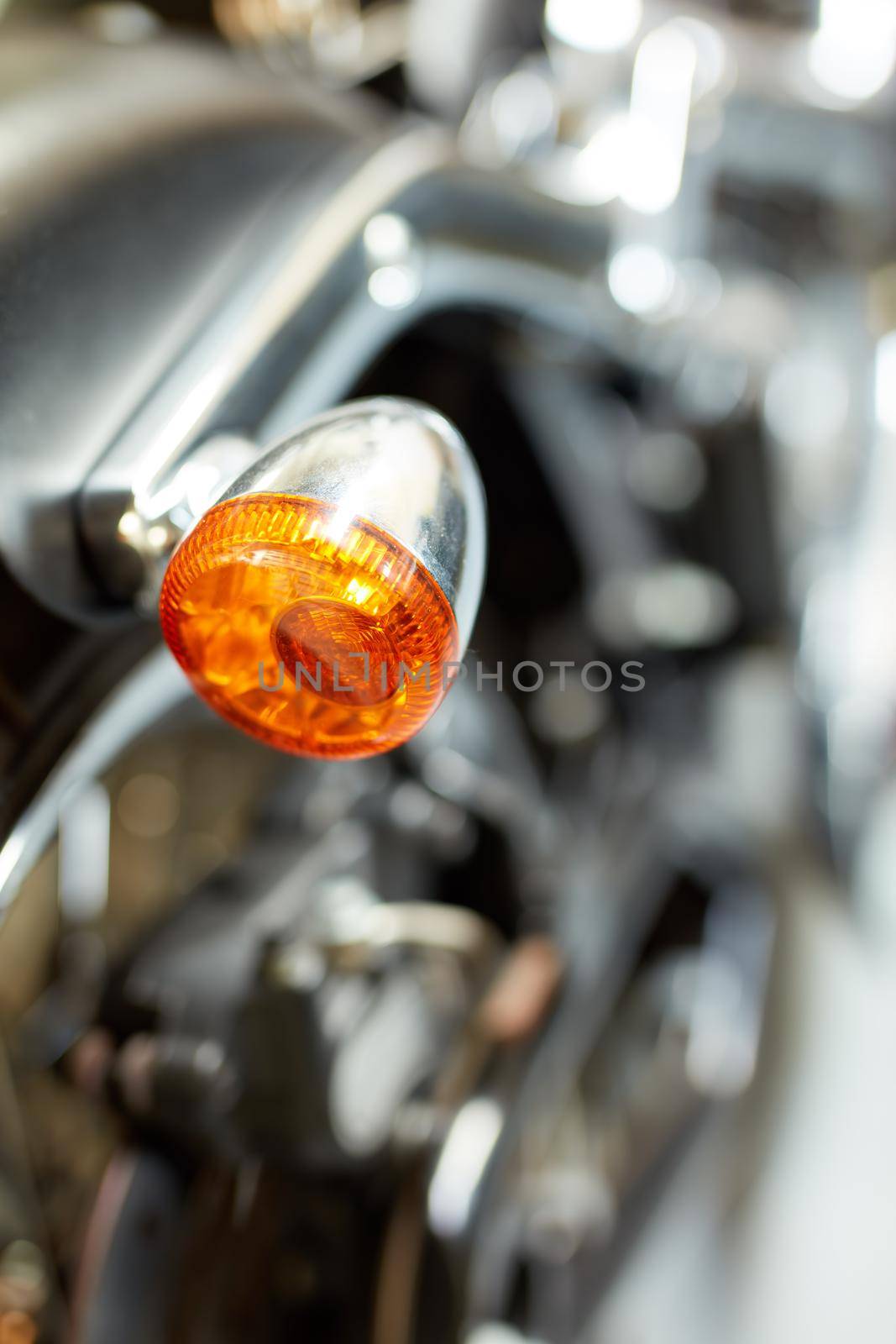 Closeup rear view of a taillight on a motorbike. Orange turning light on a blurred black vintage motorcycle. One modern chrome transportation vehicle. Maintenance on a shiny classic retro custom bike by YuriArcurs