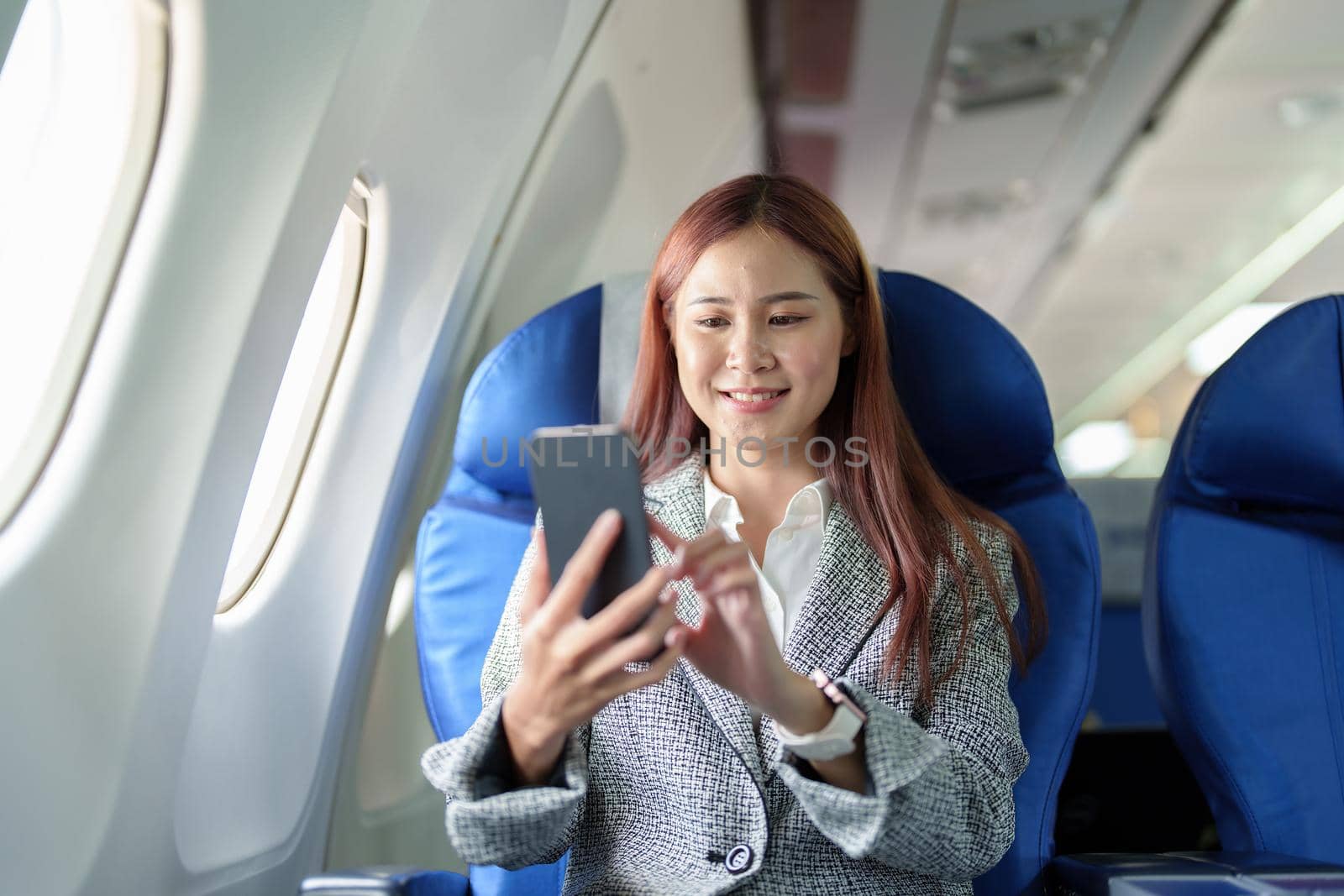 A portrait of a smiling Asian businesswoman using her phone while on a plane.