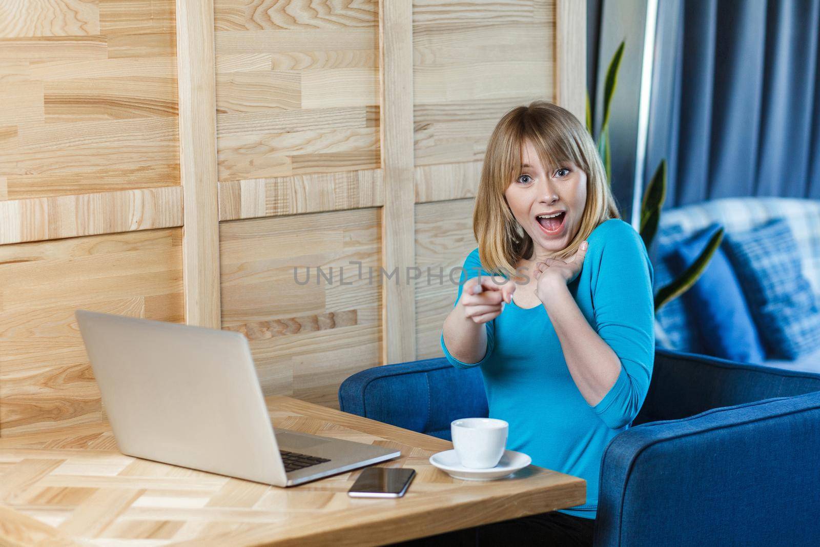 Seriously! Portrait of unbelievable young girl freelancer with blonde bob haircut hair in blue blouse are sitting in cafe, working on laptop, pointing finger to you with shocked face,looking at camera