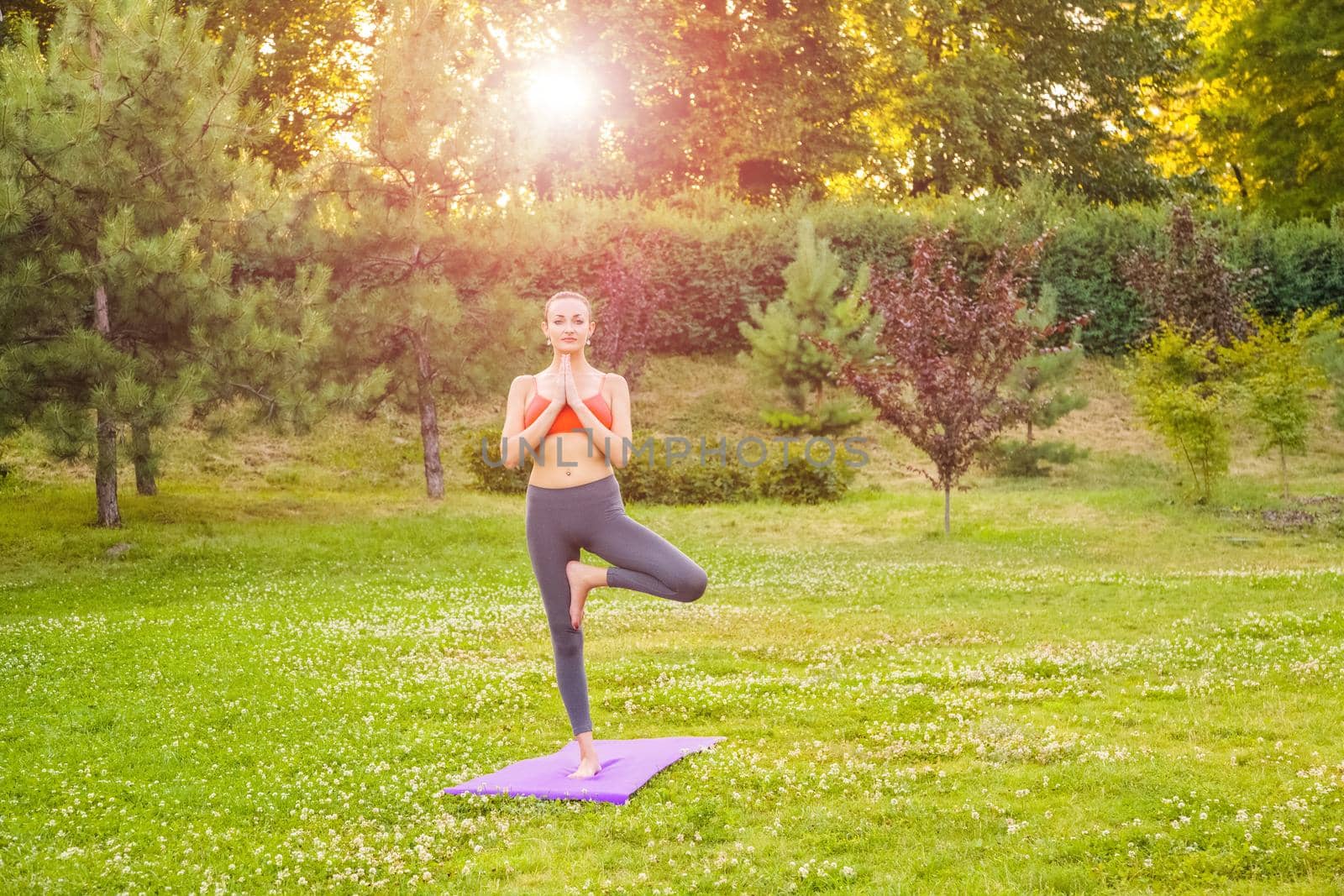 Cheerful young beautiful woman practicing and posing yoga in the park.