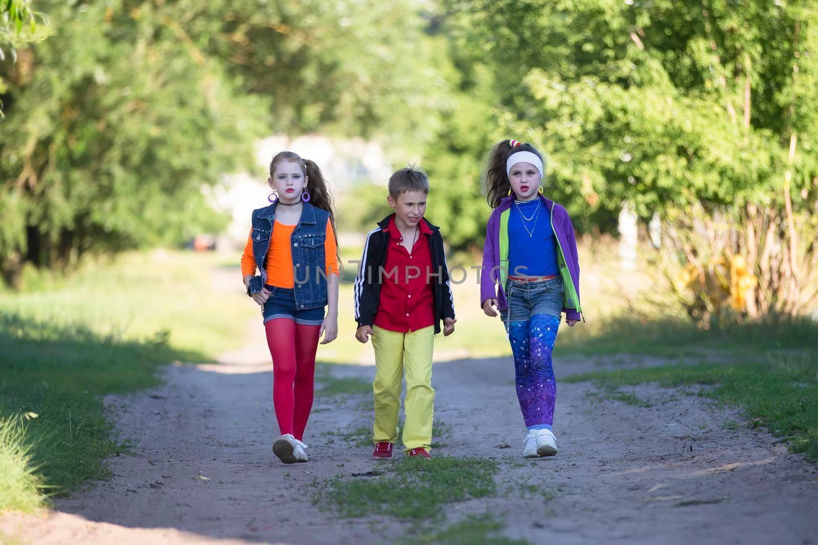 Cheerful kids a boy and two girls in cool outfits are walking along the road by Sviatlana