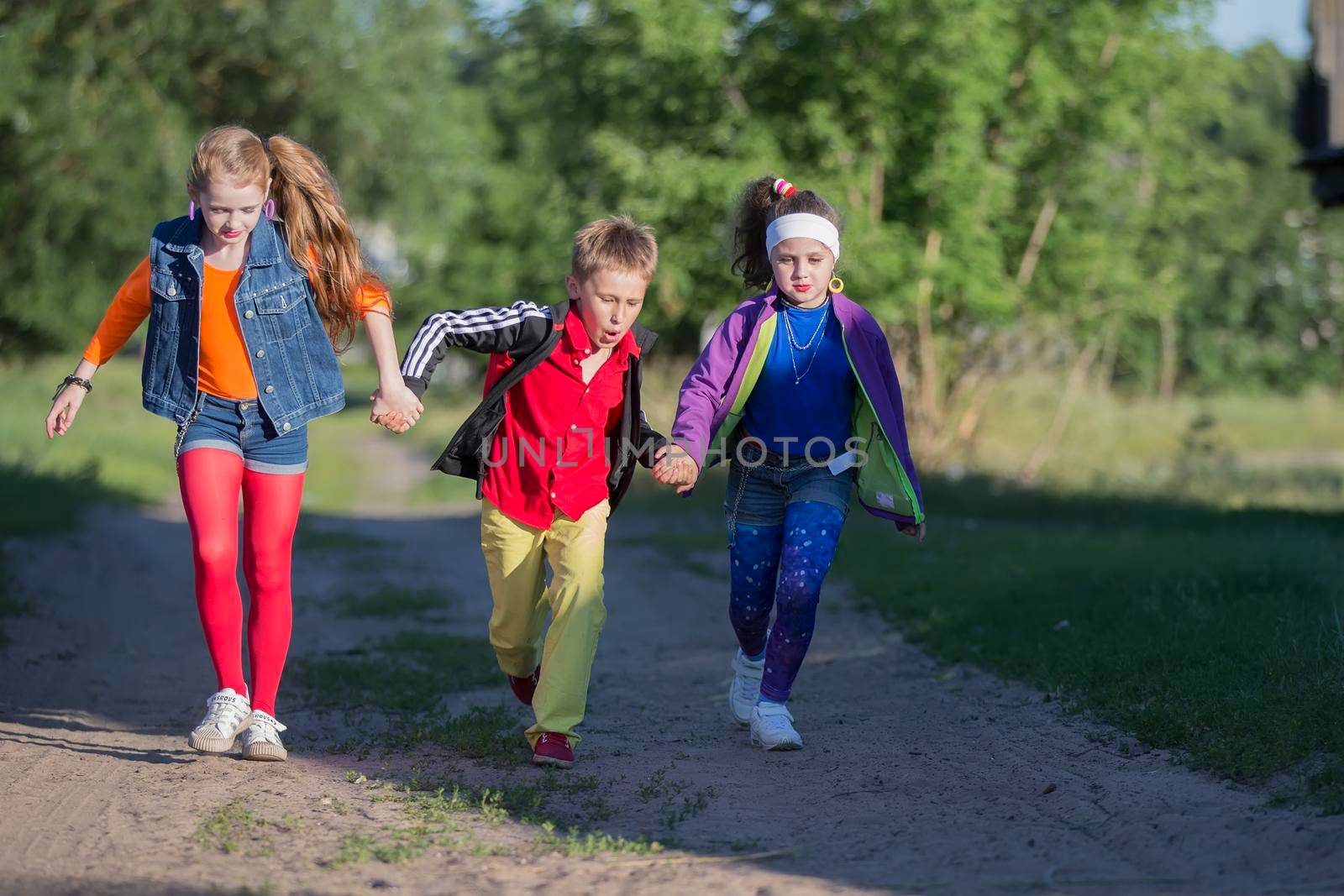 Cheerful kids a boy and two girls in cool outfits run along the road