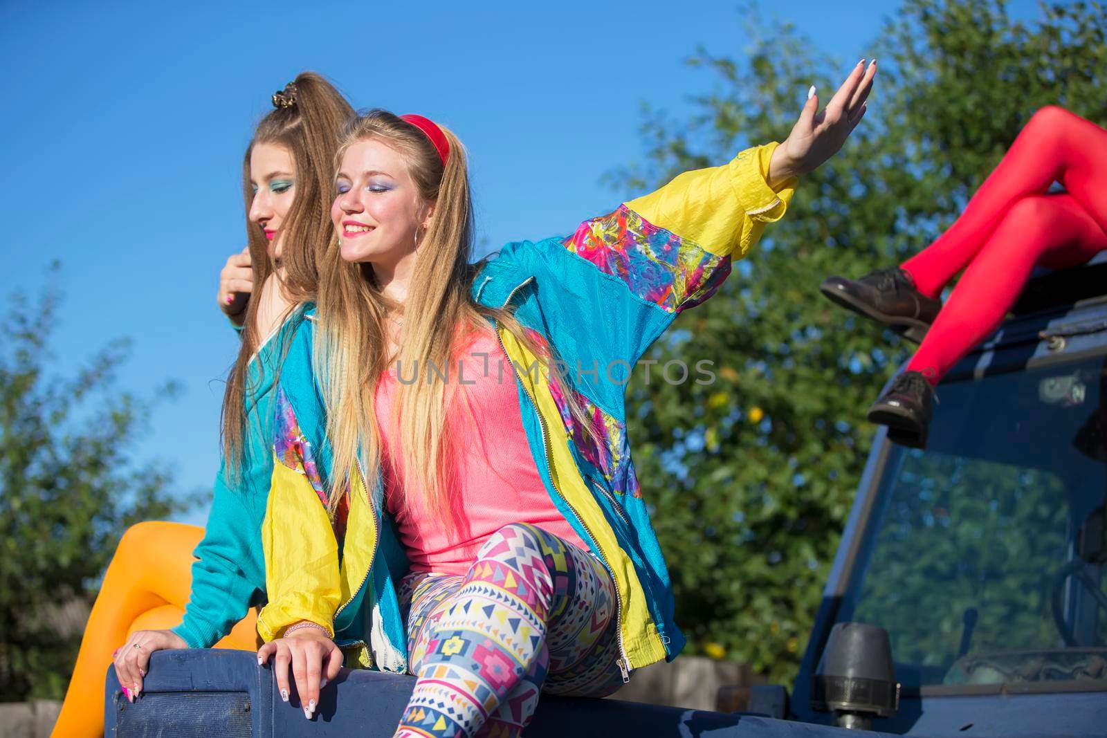 Beautiful country girls dressed in the style of the nineties sit on a tractor.