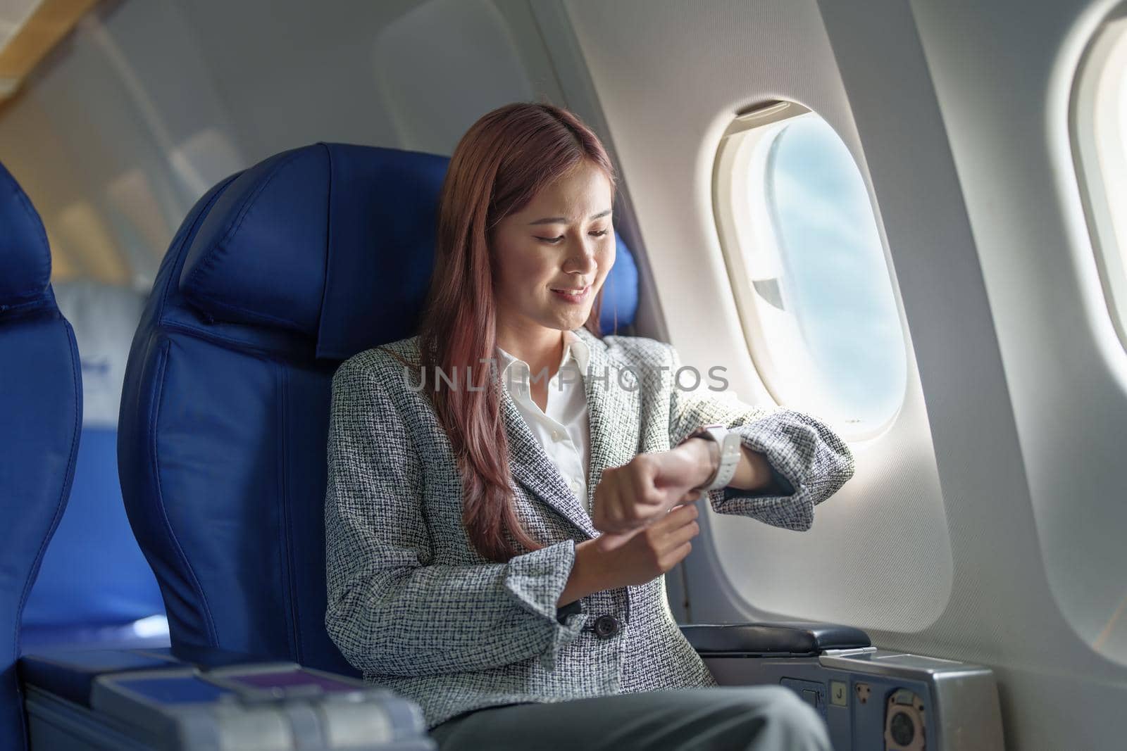 Portrait of a smiling Asian businesswoman looking at the time on the plane by Manastrong