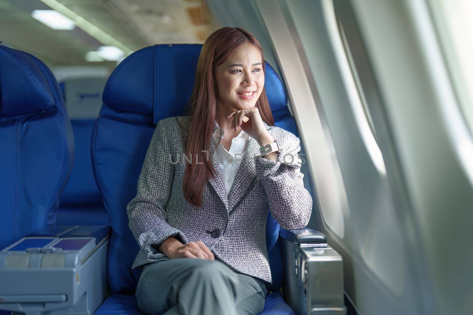 Portrait of a young Asian businesswoman smiling while riding a plane by Manastrong