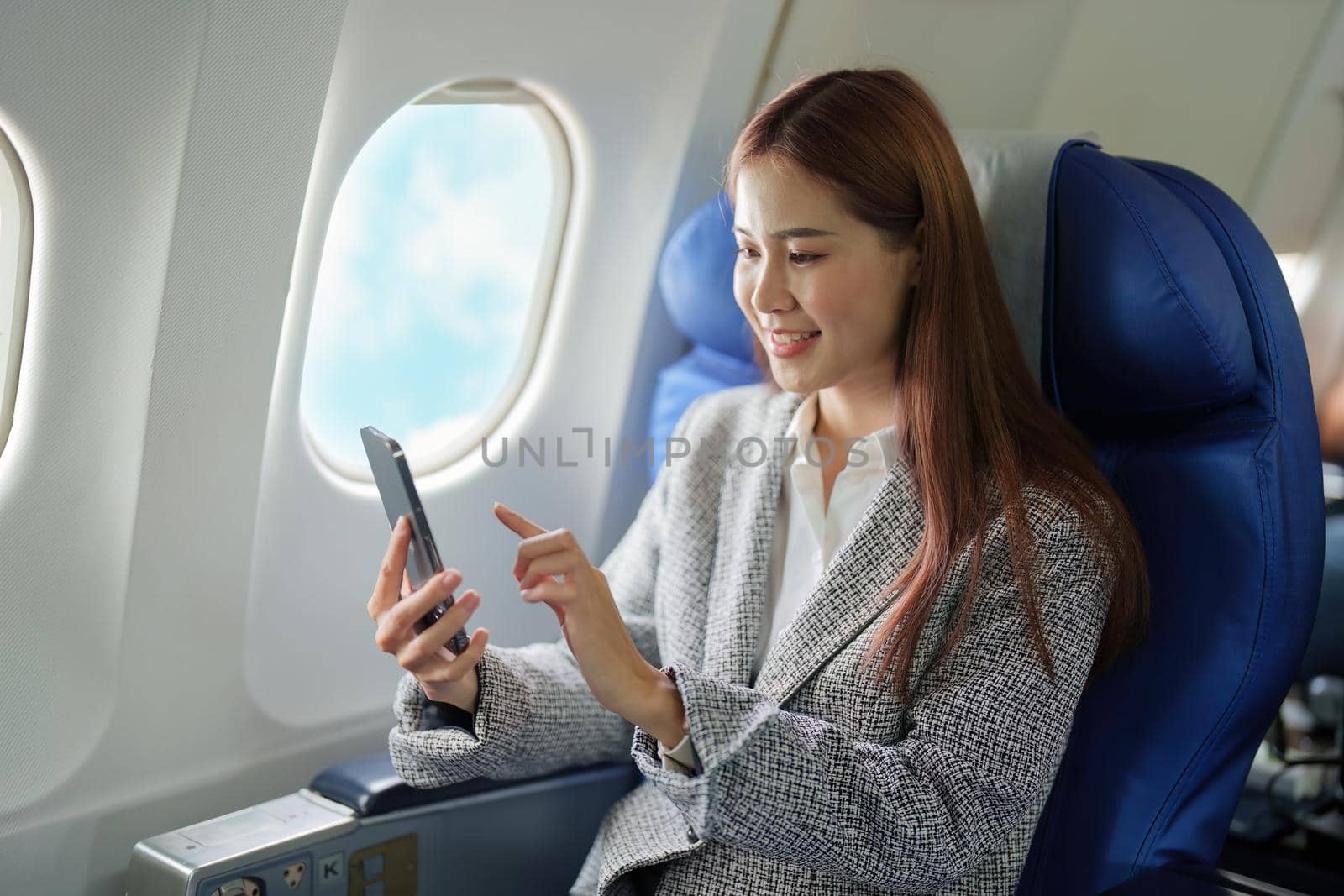 A portrait of a smiling Asian businesswoman using her phone while on a plane.